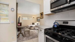 A kitchen with a stove, microwave, and white cabinets. There is a dining area with a table and chairs. - Affordable Executive Getaway — blocks to Beach and Funk Zone (Santa Barbara)