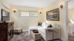 A living room with a white sofa, a small wooden table, a television, and a painting on the wall. - Affordable Executive Getaway — blocks to Beach and Funk Zone (Santa Barbara)