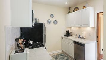A compact kitchen with white cabinets, a black stove, a dishwasher, and a small countertop.