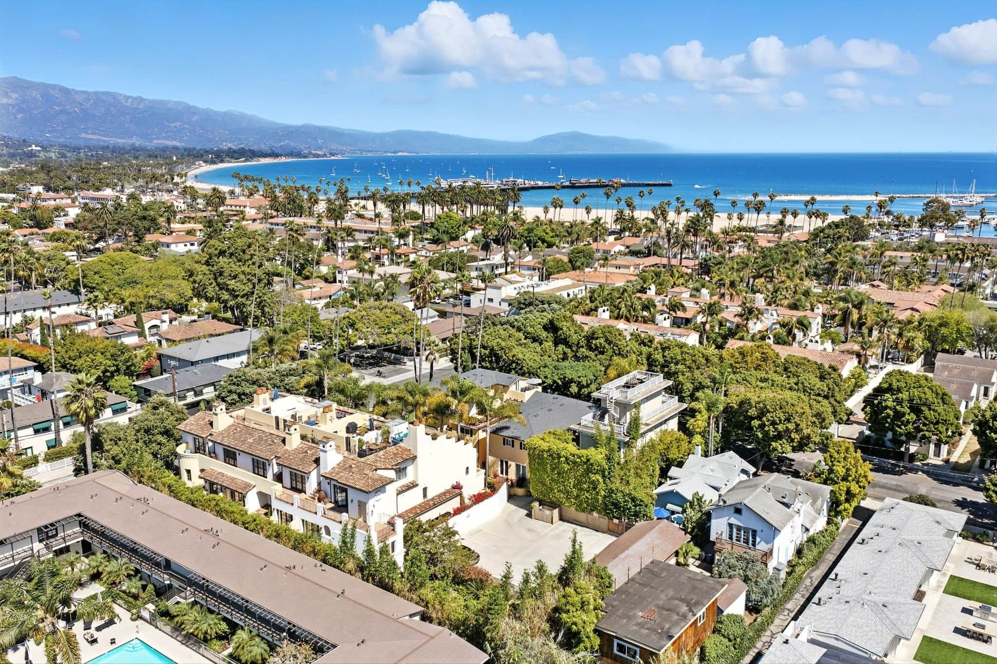 An aerial view of a coastal residential area with houses, a beach, and a pier.