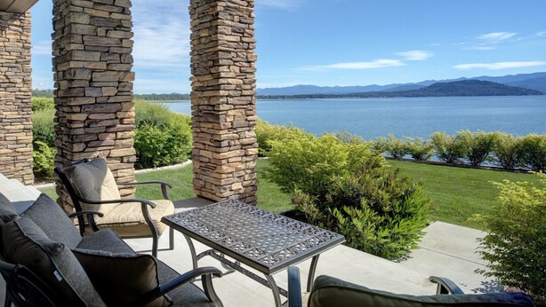 A patio with stone pillars, a table, and chairs overlooking a lake with mountains in the distance. - Townhome, Groups Welcome - Seasons at Sandpoint (Sandpoint)