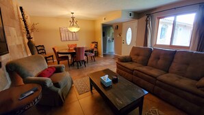 Una sala de estar con sofá, sillón, mesa de centro y comedor con sillas y mesa.