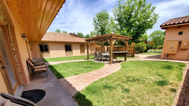 Un patio trasero con una pérgola, mobiliario de exterior y un césped bien cuidado.