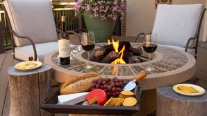 A round outdoor table with a fire pit, surrounded by two chairs, a bottle of wine, two glasses, and a tray with cheese, grapes, crackers, and bread. - Broadmoor Estate Summer Rental - Designed for unforgettable family getaways. (Colorado Springs)