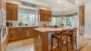 A spacious kitchen with wooden cabinets, a large island with bar stools, and a view of the outdoors through large windows. - Broadmoor Estate Summer Rental - Designed for unforgettable family getaways. (Colorado Springs)