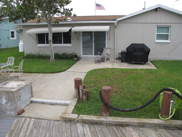 Una casa con patio, mobiliario exterior y una parrilla.