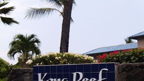 Schild für Kona Reef mit einer Steinmauer und tropischen Pflanzen.