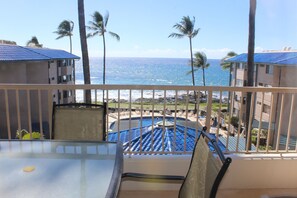 A balcony with a view of the ocean, palm trees, and a pool area. - Kona Reef F13 - Nicely Renovated - Ocean View - Free WiFi, 3 minute walk to town (Kailua Kona)