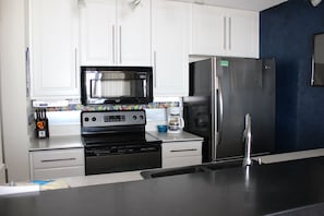 Una cocina con gabinetes blancos, un microondas negro, un refrigerador de acero inoxidable y una cafetera.