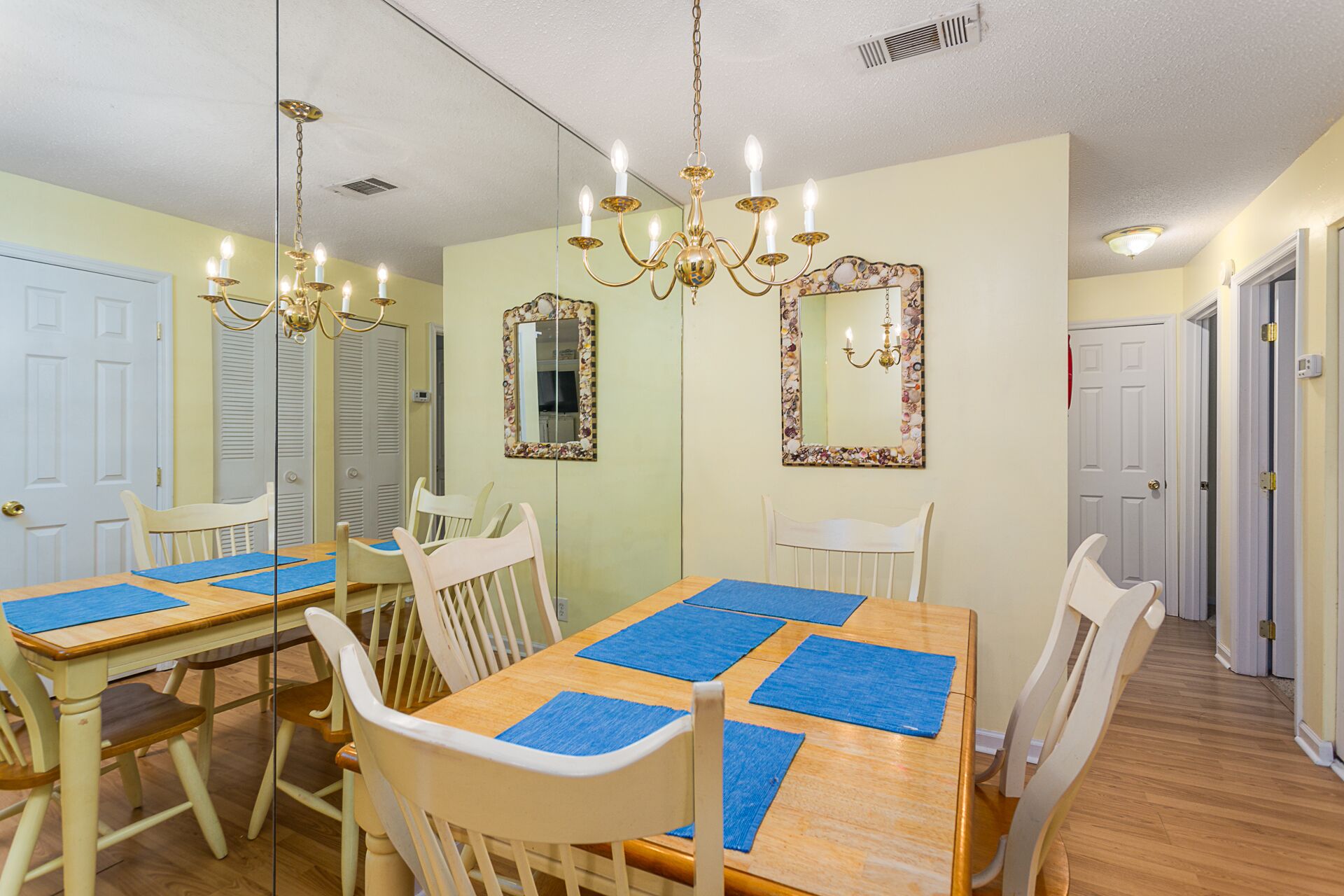 Un coin repas avec une table en bois, des chaises blanches, des sets de table bleus et un lustre.