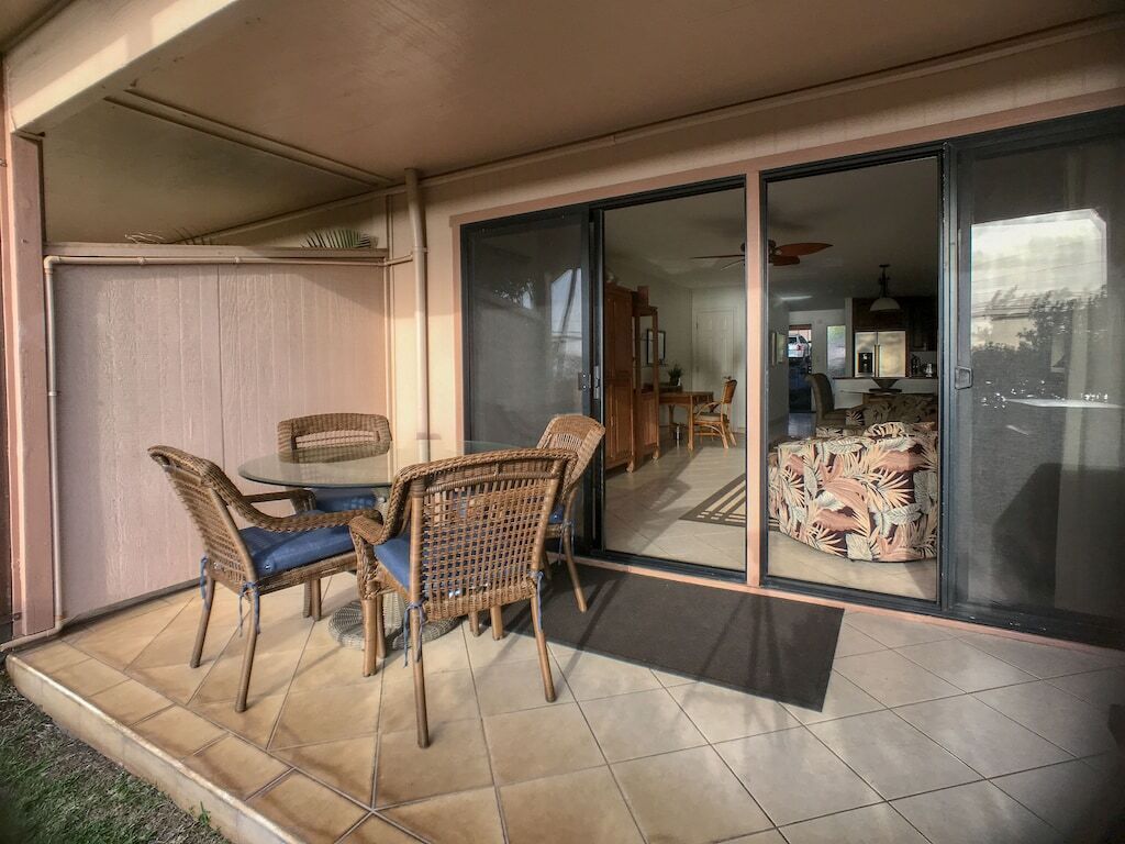 A covered patio area with wicker furniture and a glass door leading to an interior space.