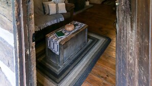 A rustic cabin interior with a stone fireplace, wooden furniture, and a chandelier.