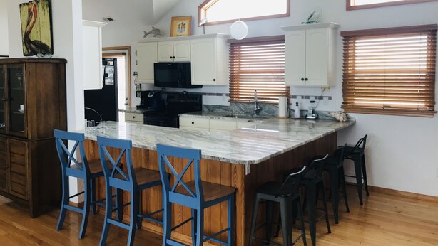 A kitchen with a large island, white cabinets, and blue bar stools. - Spacious home,saltwater heated pool, game room, volleyball,ocean views & Tennis (Corolla)