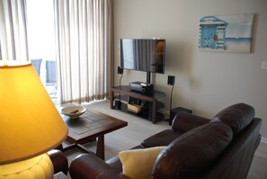 Un salon avec un canapé, une table basse, un téléviseur posé sur un meuble, une lampe et un tableau accroché au mur.