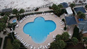 Oversigtsbillede af et resort med en central swimmingpool, omgivet af liggestole og palmer.
