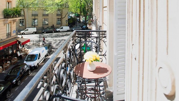 A balcony with a view of the Eiffel Tower, a street with parked cars, and a tree-lined street. - Stunning & Spacious in Superb Location with Balcony & Eiffel Views (Paris)