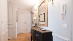 A hallway with a wooden floor, a black dresser with drawers, a large mirror, and a wall-mounted telephone. - Stunning & Spacious in Superb Location with Balcony & Eiffel Views (Paris)
