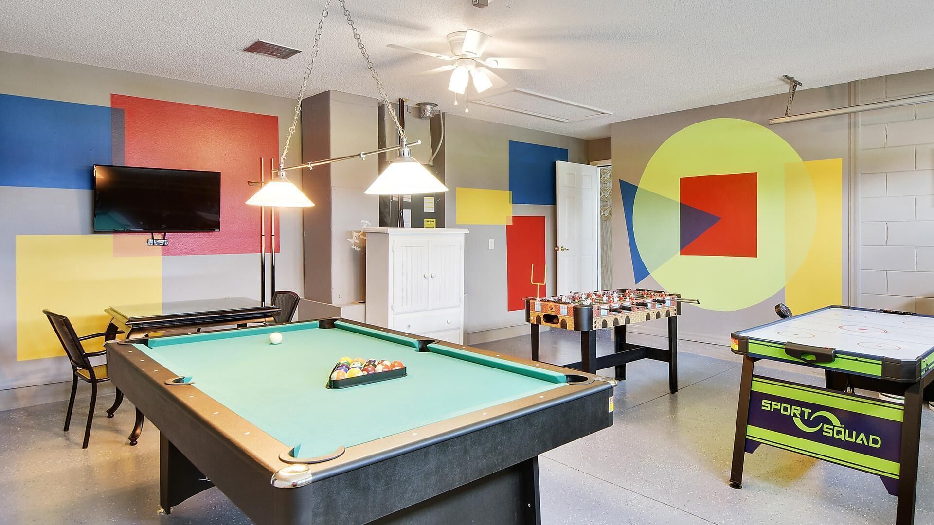 A recreational room with a pool table, foosball table, and a table tennis table.