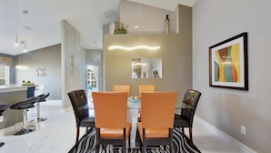 Un comedor moderno con una mesa de vidrio y sillas de cuero, una cocina con barra y un espejo grande en la pared.