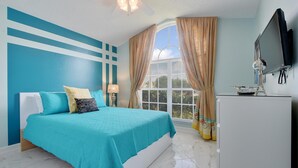 Un dormitorio con cama, televisión, lámpara y ventana con cortinas.