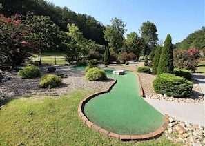 Un campo da minigolf con un manto erboso sinuoso, circondato da aree verdi curate e alberi.