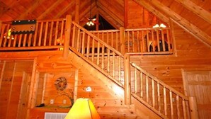 Un intérieur en bois avec un escalier menant à un niveau supérieur, un ventilateur de plafond et une guirlande décorative.