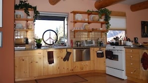 A kitchen with wooden cabinets, a stove, and shelves with dishes. - Cozy Adobe with Hot Tub and Fabulous Views in Outdoor Paradise. (Castle Valley)