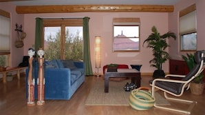 A cozy living room with a blue sofa, a wooden coffee table, and a black leather chair. There are two windows with curtains, a lamp, and a plant. - Cozy Adobe with Hot Tub and Fabulous Views in Outdoor Paradise. (Castle Valley)
