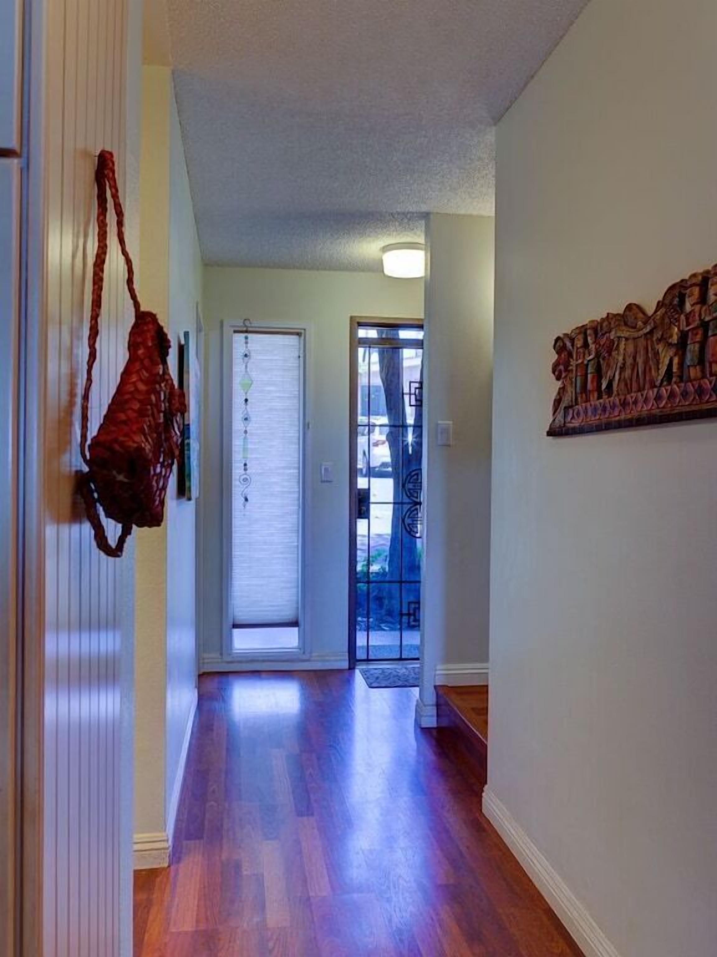 A hallway with wooden flooring, a door with a window, and a wall-mounted artwork.