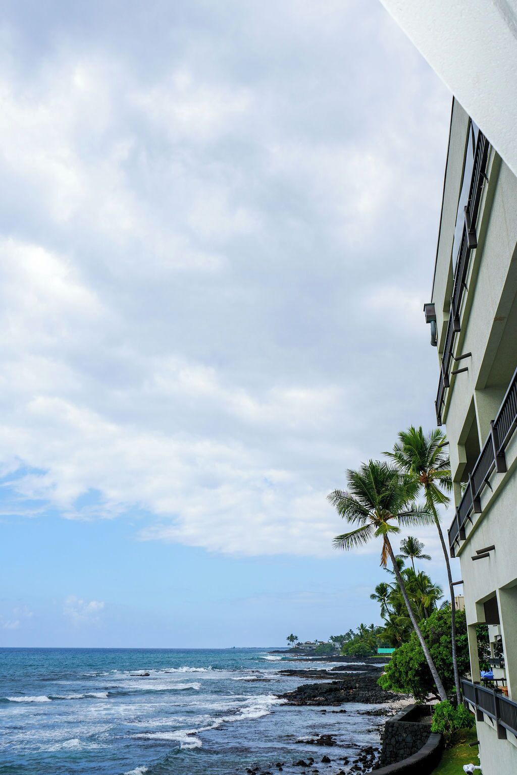 Eine Küstenansicht mit einem Gebäude direkt am Meer, inklusive Balkonen und blauem Himmel.
