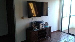 Ein Zimmer mit einem an der Wand befestigten Flachbildfernseher, einer Holzkabine mit Drucker und Dekoration sowie einem Fliesenboden.