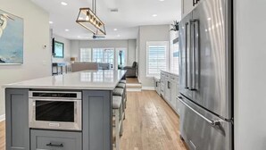 A modern kitchen with a large island, stainless steel appliances, and a dining area with a view. - Surfin' Sea | 1 PM Check In! | Modern Updated Gulf-Front Home | Private Pool | FREE Beach Chairs Within Steps | 6-Seat Golf Cart Included! | Stunning Views! (Miramar Beach)