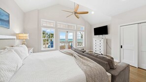 A bedroom with a large bed, a ceiling fan, a TV, and a view of the beach. - Surfin' Sea | 1 PM Check In! | Modern Updated Gulf-Front Home | Private Pool | FREE Beach Chairs Within Steps | 6-Seat Golf Cart in Garage! | Stunning Views! (Miramar Beach)