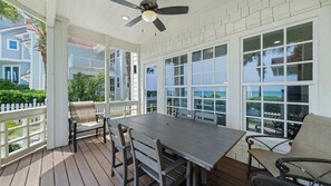 A covered outdoor area with a table and chairs, large windows, and a ceiling fan. - Surfin' Sea | 1 PM Check In! | Modern Updated Gulf-Front Home | Private Pool | FREE Beach Chairs Within Steps | 6-Seat Golf Cart in Garage! | Stunning Views! (Miramar Beach)