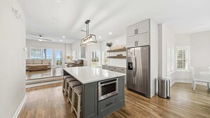 A modern kitchen with a central island, stainless steel appliances, and a view to the living area. - Surfin' Sea | 1 PM Check In! | Modern Updated Gulf-Front Home | Private Pool | FREE Beach Chairs Within Steps | 6-Seat Golf Cart Included! | Stunning Views! (Miramar Beach)