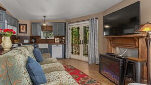 A living room with a sofa, a fireplace, a television, and a kitchen in the background. - Hot tub, Propane fire pit, Interact with animals, Privacy, 10 miles from AVL. (Fairview)