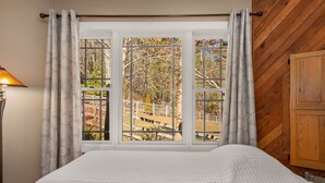 A bedroom with a bed, a window with curtains, a lamp, and a wooden wall. - Hot tub, Propane fire pit, Interact with animals, Privacy, 10 miles from AVL. (Fairview)