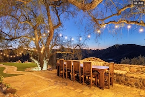 An outdoor dining area with a stone wall, wooden chairs, and a table under string lights.
