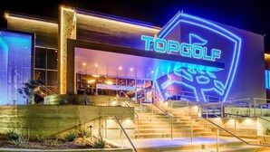 A building with a neon sign reading "TOPGOLF" and a staircase leading to the entrance.