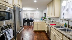 A modern kitchen with stainless steel appliances, wooden flooring, and light-colored cabinetry.