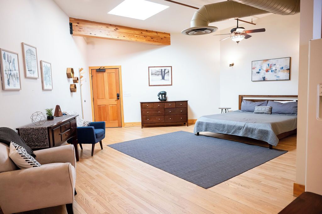 Un dormitorio con cama, escritorio, silla, cómoda y obras de arte en las paredes.