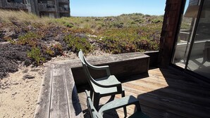 A wooden deck with outdoor furniture, a sandy beach, and a building with large windows in the background. - Pajaro Dunes Vacation Home on Epic Private Beach for family or Romantic Getaway (Watsonville)