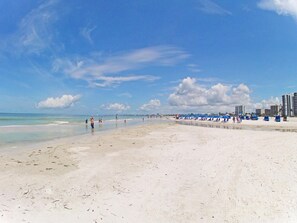 A wide sandy beach with a clear sky and distant buildings. - Upscale Top-Floor Condo W/Gulf View, Sugary Sand Beach (Fort Myers Beach)