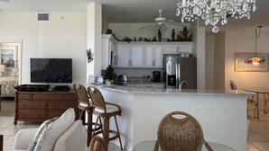 A modern kitchen with white cabinets, a stainless steel refrigerator, and a chandelier. - Upscale Top-Floor Condo W/Gulf View, Sugary Sand Beach (Fort Myers Beach)