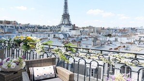 A balcony with wicker furniture and flower arrangements, overlooking a cityscape with the Eiffel Tower in the background. - Dream-Come-True With Breathtaking Eiffel & Paris Views + Terrace (Paris)