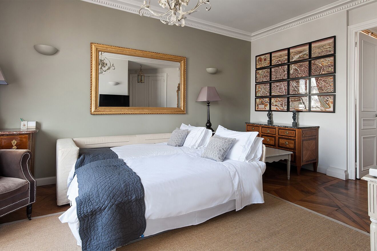 Quarto com uma cama grande, cômoda, cadeira, espelho e parede com quadros.