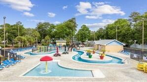 Un área de piscina con varias piscinas, sillas de descanso y un pequeño edificio.
