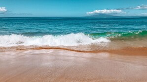 Une plage avec une eau d’un bleu limpide et des vagues.