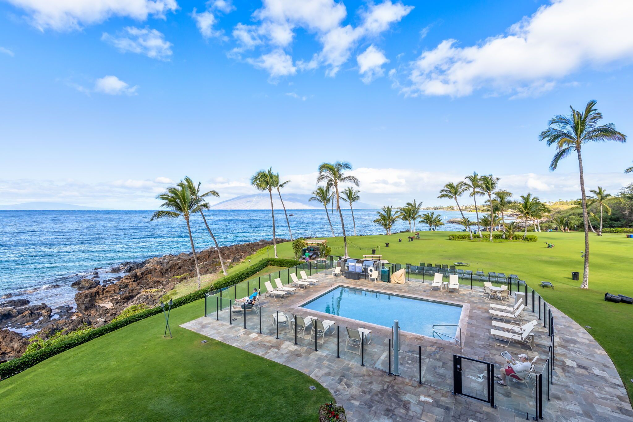A pool area with lounge chairs and a view of the ocean.