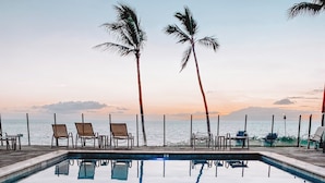 Une piscine à l’eau claire où se reflètent les palmiers, avec une vue imprenable sur le coucher de soleil.